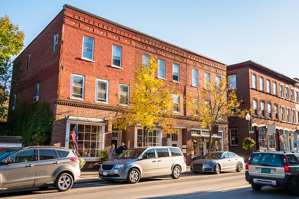 Traditional American brick buildings with shops along a busy street at sunset. Woodstock, VT, USA.