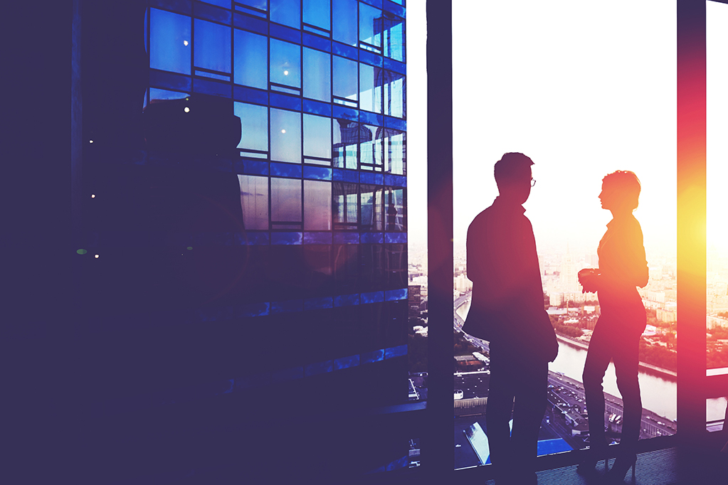 Silhouette of a two successful managing directors discuss ideas after meeting with partners while standing near big office window, young man and woman skilled economists relaxing after conference